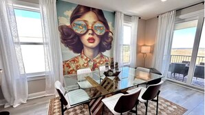 A dining area with a glass table, chairs, and a mural on the wall.