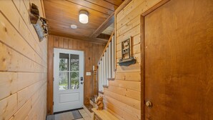 Un couloir en bois avec un banc, une porte et une petite étagère ornée d’objets décoratifs.