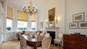 A dining room with a large wooden table, six chairs, a chandelier, a fireplace, and framed artwork on the walls. - The Kensington Townhouse, by Veeve (London)