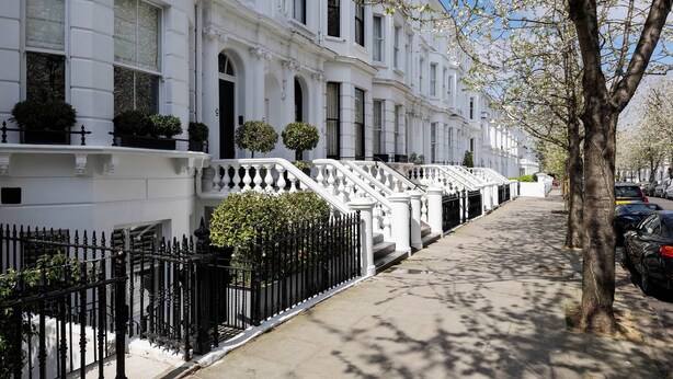 A row of white townhouses with black iron railings and a tree in the foreground. - The Kensington Townhouse, by Veeve (London)