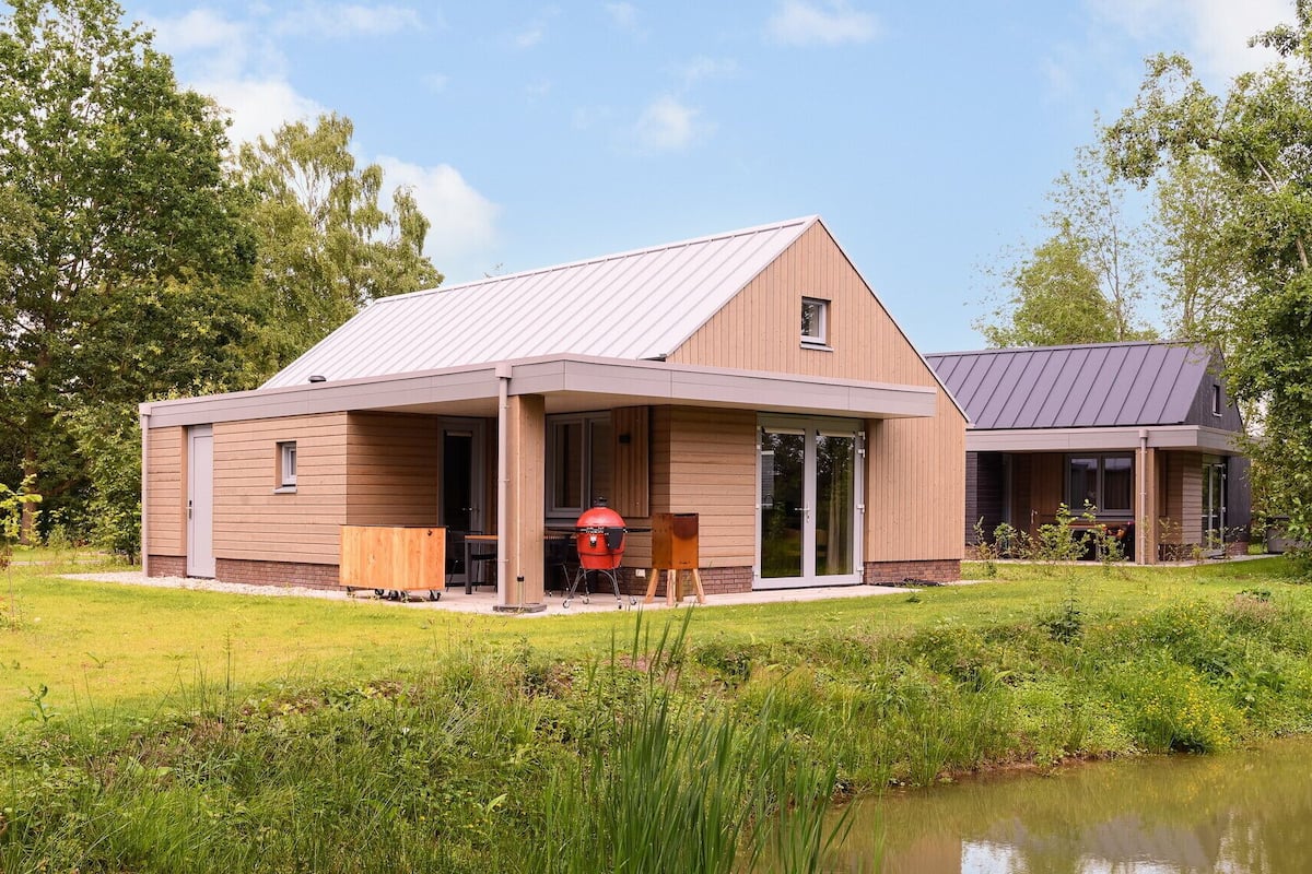 A modern two-story house with a covered patio and a pond in the foreground.