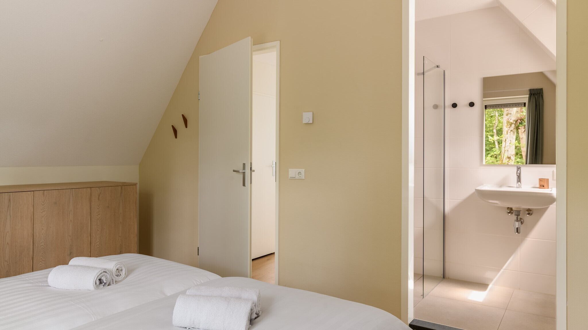 A bedroom with a bed, a wooden wardrobe, and a bathroom with a shower and sink.