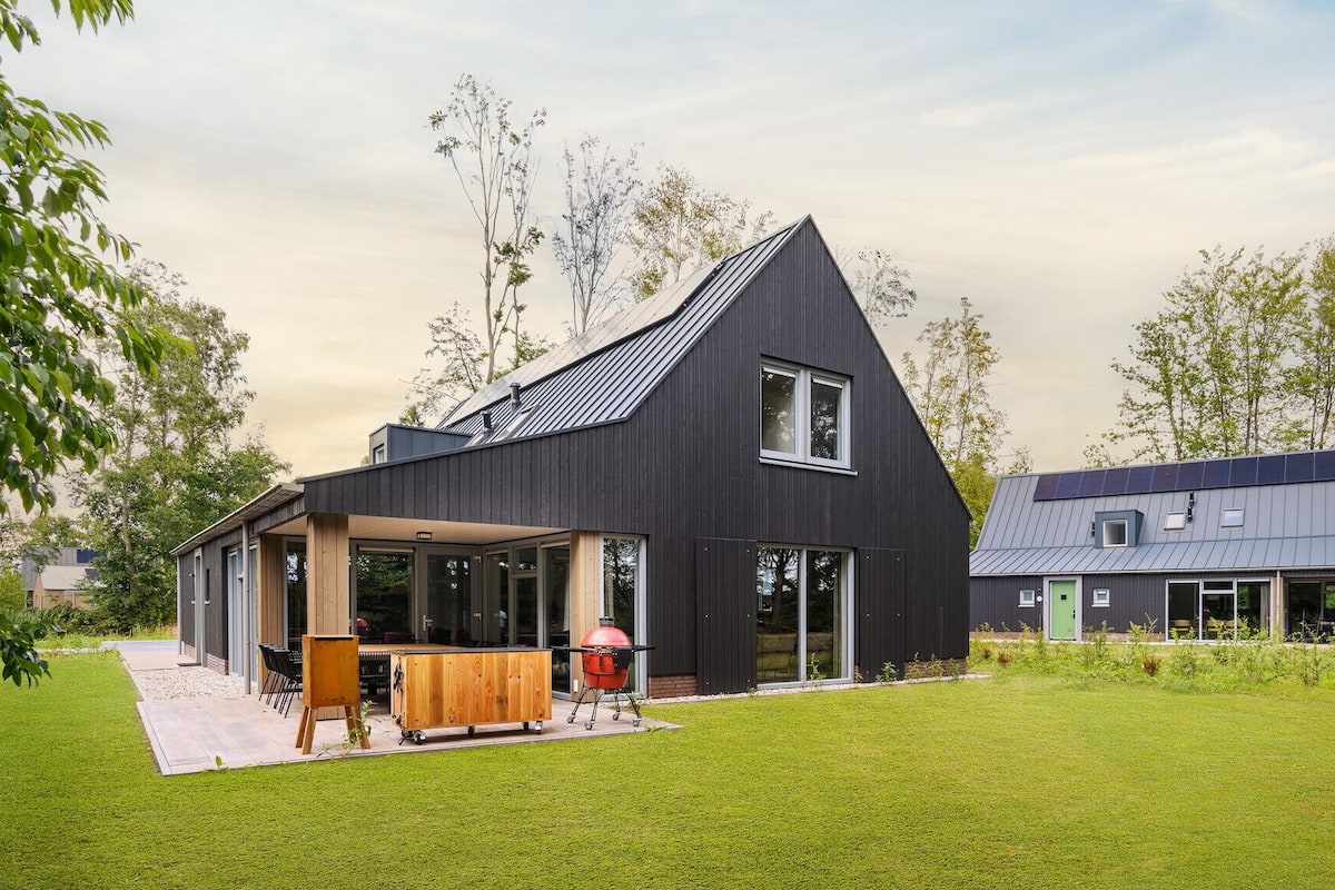 A modern house with a large patio area, a covered outdoor kitchen, and a separate building with a sloped roof.