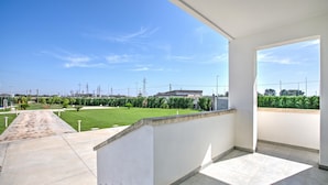 A balcony with a view of a well-maintained lawn and distant buildings. - Boutique Apartament With Pool and Padel Court (Galatina)