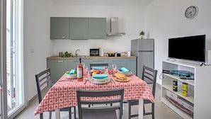 A compact kitchen with grey cabinets, a microwave, and a refrigerator. A dining table with a red and white checkered tablecloth is set with plates, a bottle, and a bowl. - Boutique Apartament With Pool and Padel Court (Galatina)