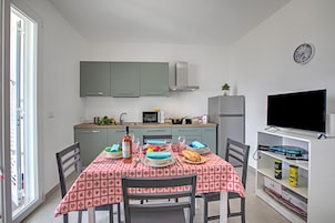 Una cocina compacta con gabinetes grises, un microondas y un refrigerador. Una mesa de comedor con mantel a cuadros rojo y blanco está servida con platos, una botella y un tazón.