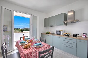 A modern kitchen with a dining area, featuring a table set for two, a built-in oven, and a view through the open sliding door. - Boutique Apartament With Pool and Padel Court (Galatina)
