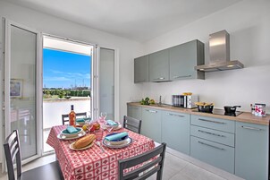 Una cocina moderna con comedor, con una mesa lista para dos personas, horno empotrado y vistas a través de puertas correderas abiertas.