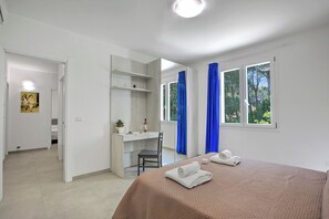 A hotel room with a bed, a desk, a chair, a window with curtains, and a door leading to another room. - Boutique Apartament With Pool and Padel Court (Galatina)