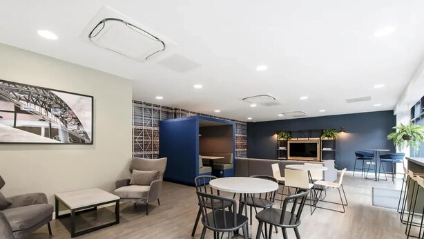 A modern lounge area with a round table, multiple chairs, sofas, and a large TV screen. - Student Only Knoll Court (Newcastle-upon-Tyne)