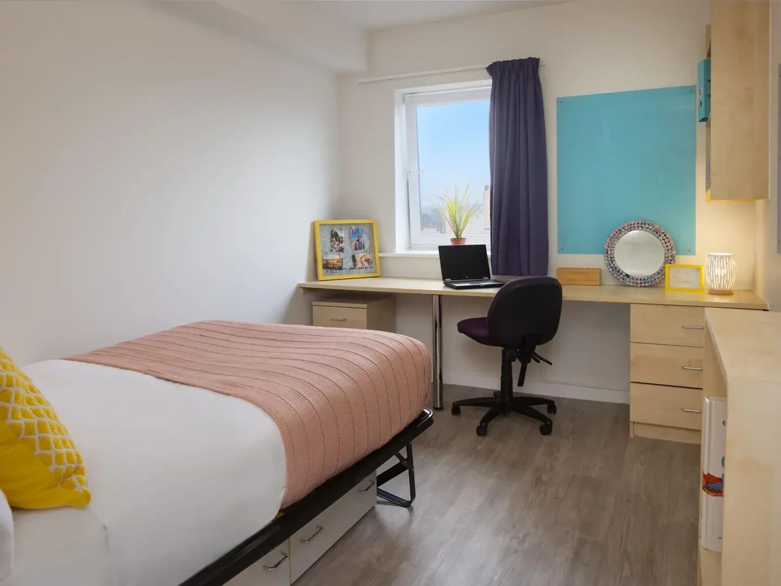 Un dormitorio con una cama, un escritorio con un ordenador portátil, una silla y una ventana con cortinas.