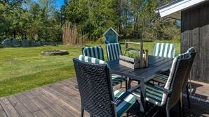 Una terraza al aire libre con una mesa y sillas, rodeada de una cubierta de madera y un césped.