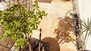 Un patio exterior con suelo de piedra, mobiliario de mimbre y plantas en macetas.