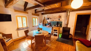Una habitación acogedora con suelo de madera, una mesa redonda con sillas de comedor, un sofá, una zona de cocina con fregadero y estufa, y un televisor montado en la pared.