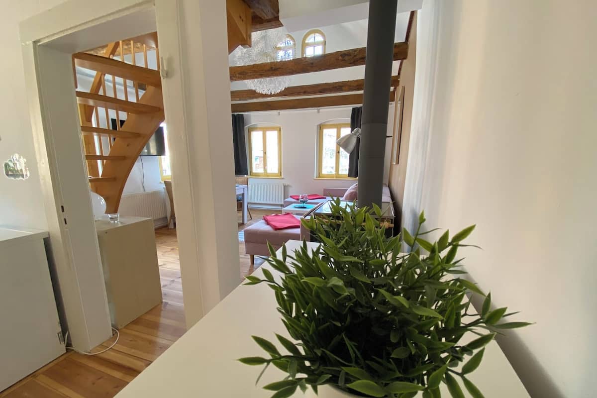 Ein Zimmer mit einem weißen Tisch, einem Blumentopf, Holzbalken, einem Fenster und einer Heizung.