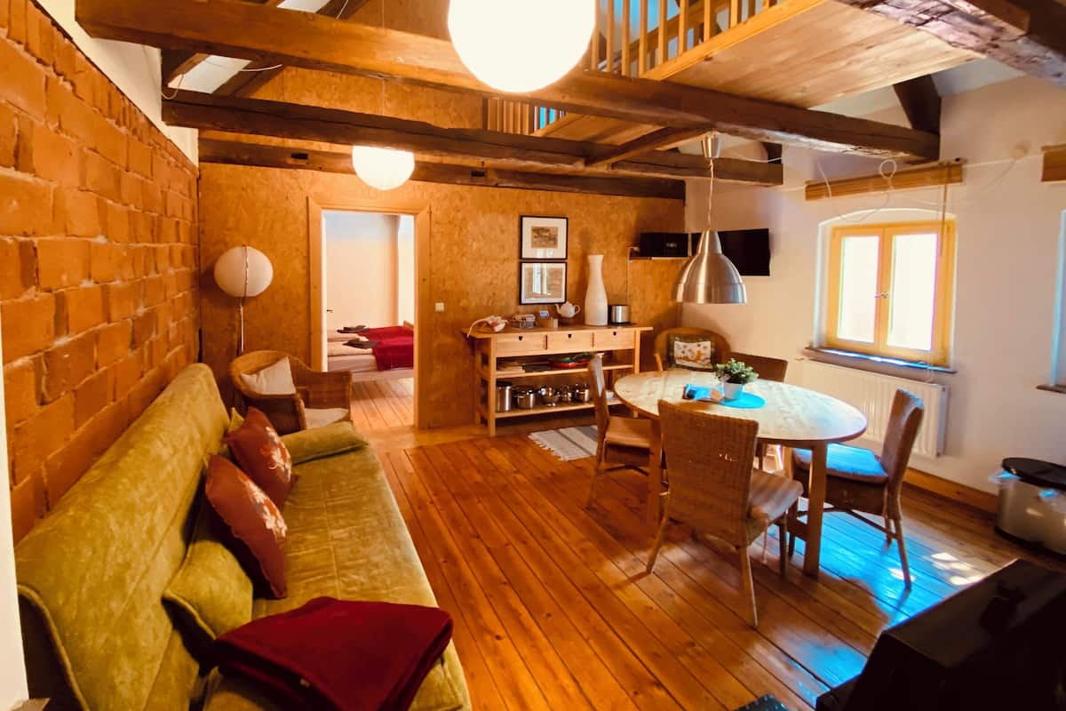 Ein gemütliches Wohnzimmer mit Holzbalkendecke, einem runden Esstisch und einer Couch mit Kissen.