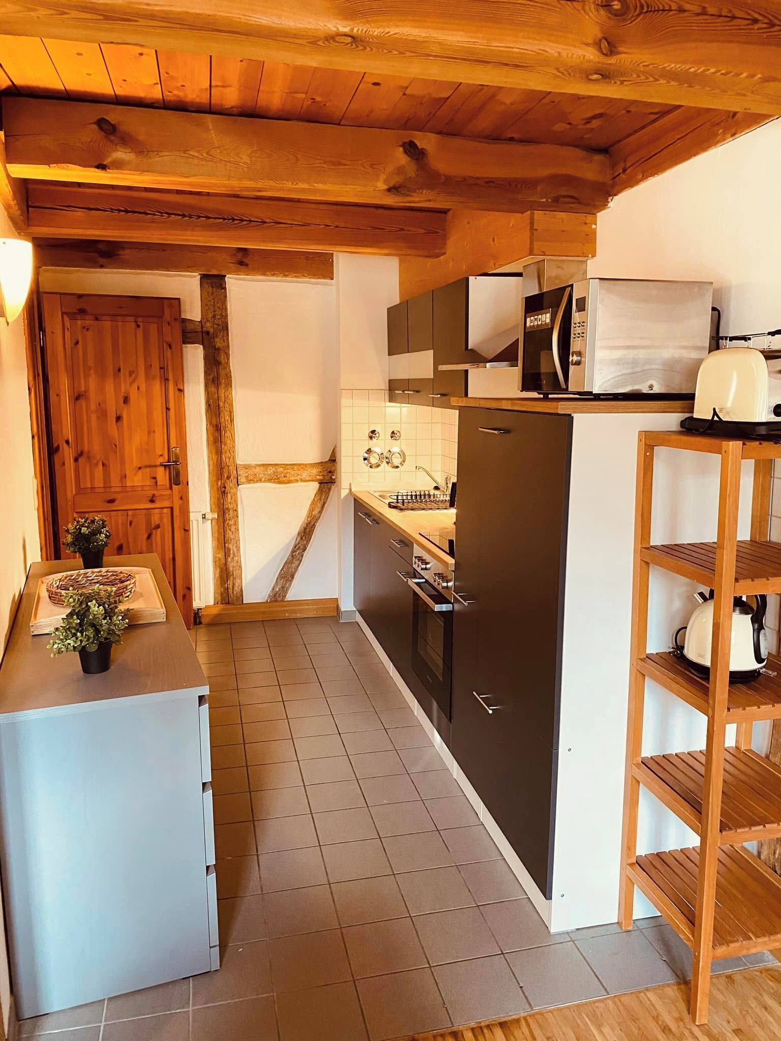 A compact kitchen with wooden beams, a refrigerator, a microwave, and a toaster.