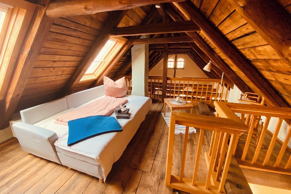Ein gemütliches Schlafzimmer im Dachgeschoss mit einem weißen Sofa, einem kleinen Tisch und einem Holengeländer.