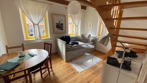 Una sala acogedora con suelo de madera, un sofá, una mesa de comedor con sillas y una escalera.