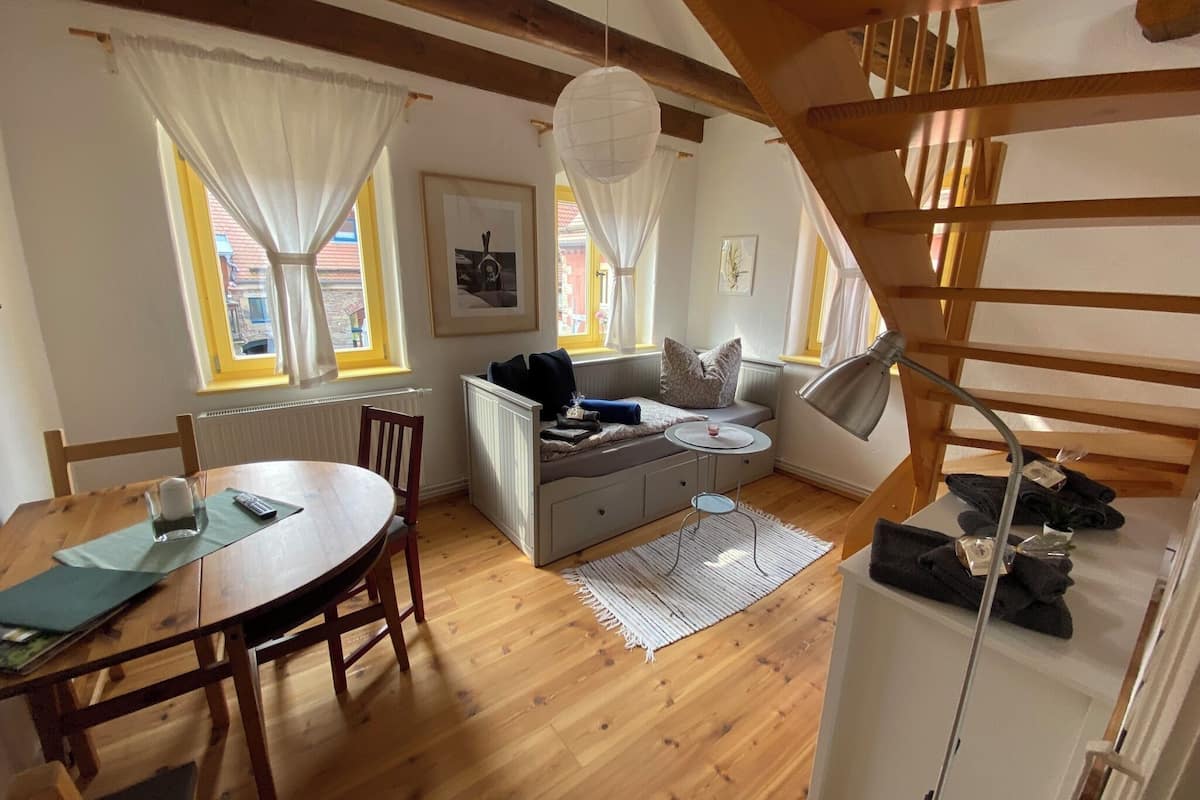 Ein gemütlicher Wohnbereich mit Holzboden, einer Couch, einem Esstisch mit Stühlen und einer Treppe.