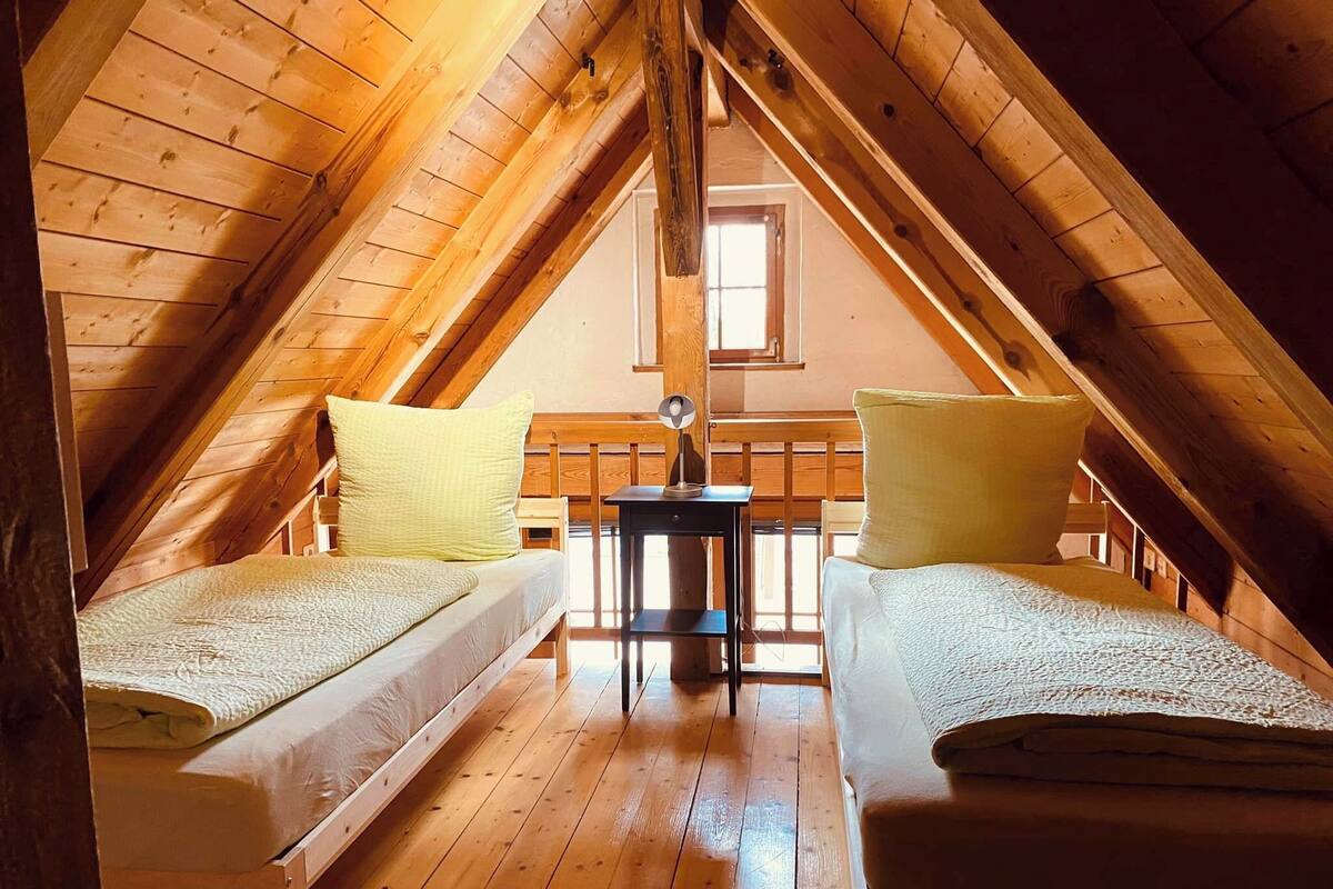 Ein gemütliches Schlafzimmer im Dachgeschoss mit zwei Einzelbetten, Holzbalken, einem kleinen Tisch und einem Fenster.