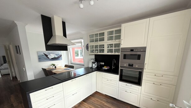 A modern kitchen with white cabinets, black countertops, and a wooden floor.