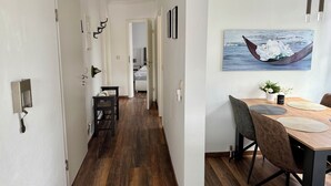 A modern hotel room with a wooden floor, a dining area with a table and chairs, and a painting of a boat on the wall.