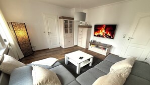A modern living room with a grey sofa, white coffee table, and a TV displaying a fireplace.