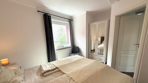 A bedroom with a bed, a window with curtains, a radiator, a wardrobe, and a door.