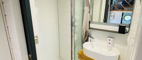Un baño moderno con ducha envuelta en vidrio, un lavabo blanco con encimera de madera y un espejo sobre el lavabo.