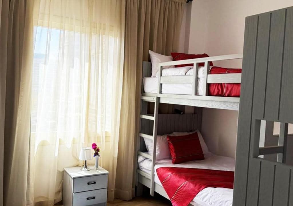 A bedroom with a bunk bed, a bedside table with a lamp, and a window with sheer curtains.