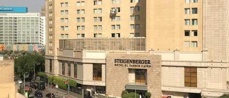 A large hotel with multiple floors, a prominent entrance, and a parking area in front.