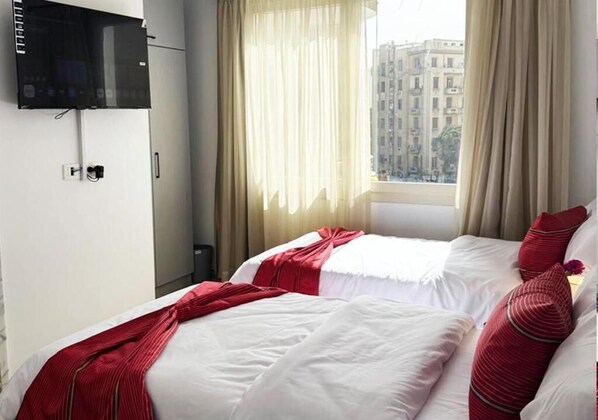 A hotel room with two beds, a TV mounted on the wall, and a window with curtains.