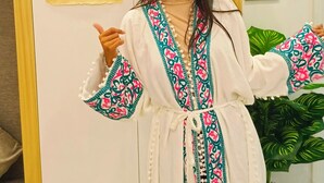 A person in a white robe with colorful patterns standing in front of a wall with framed artwork. - marhaba inn (Cairo)