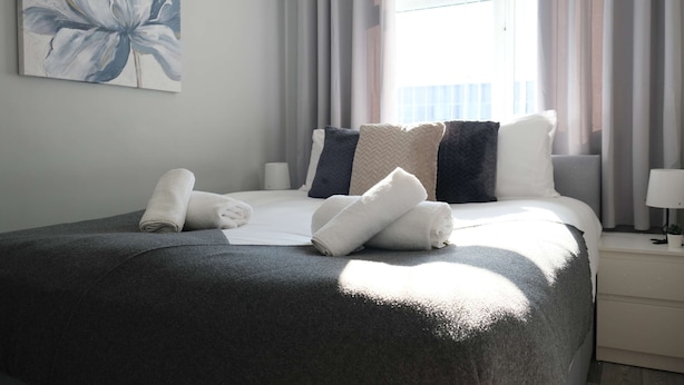 A neatly made bed with a grey blanket, white pillows, and rolled towels. - Modern 3BR Family Home w/ Garden | Luton (Luton)