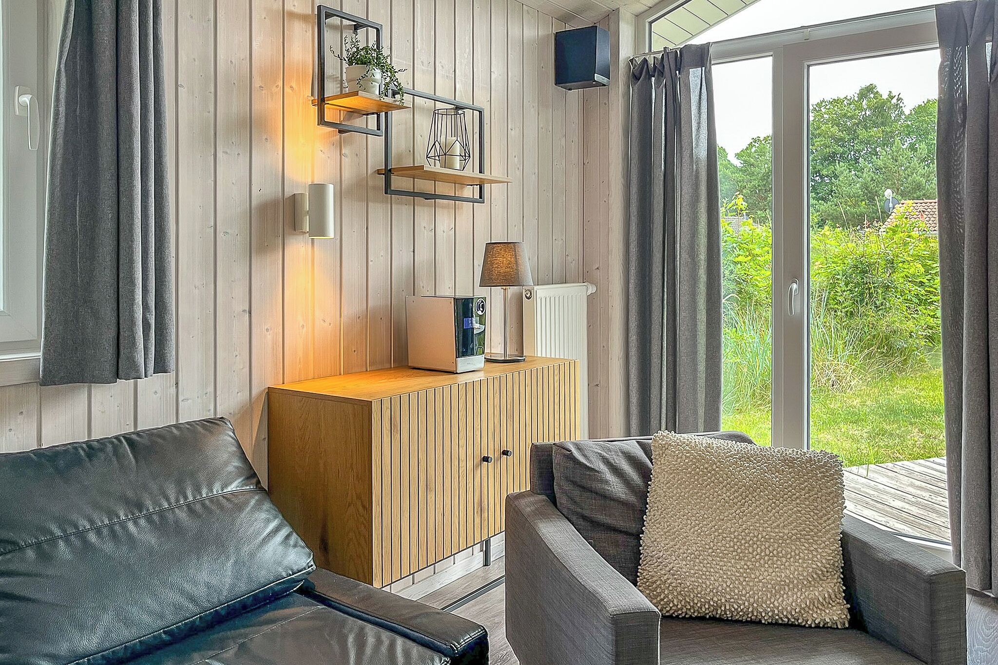 Een moderne woonkamer met een houten kast, een bank en uitzicht op groen via een glazen deur.