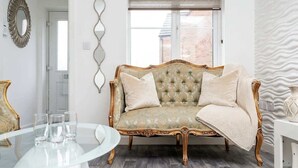 A room with a tufted sofa, a glass table with glasses, a mirror, and a patterned wall. - Spacious 3BR Garden House near Central Doncaster (Doncaster)