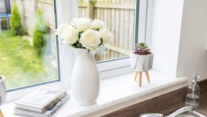 A white vase with white flowers on a windowsill, a small potted plant, and a stack of books. - Spacious 3BR Garden House near Central Doncaster (Doncaster)