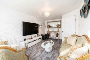 A modern living room with a flat-screen TV, a white entertainment unit, a round coffee table, and a patterned sofa. - Spacious 3BR Garden House near Central Doncaster (Doncaster)