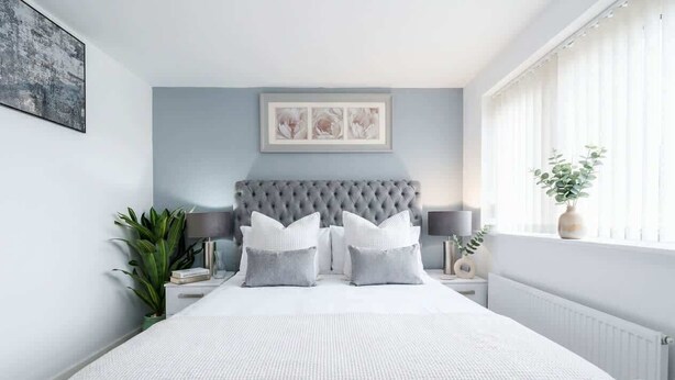 A bedroom with a large bed, a tufted headboard, bedside tables with lamps, and a window with curtains. - Spacious 3BR Garden House near Central Doncaster (Doncaster)