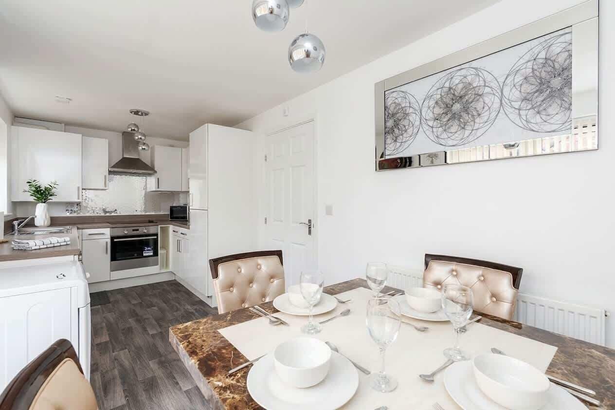 Een moderne keuken met witte kasten, een marmeren aanrechtblad en een eethoek met een tafel voor vier personen.