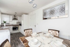 A modern kitchen with white cabinetry, a marble countertop, and a dining area with a table set for four.