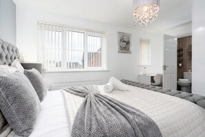 Une chambre à coucher avec un grand lit, un lustre, une fenêtre avec des stores et une porte donnant sur une salle de bain.