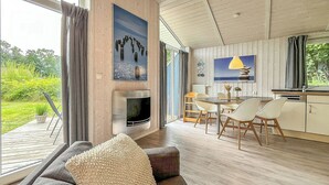 A modern living room with a large window, a fireplace, a dining area, and a kitchen. - Pulverhorn vacation home 03 (Lübeck-Travemünde)