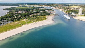 An aerial view of a coastal town with a large cruise ship docked at the harbor, surrounded by residential areas and a sandy beach. - Pulverhorn vacation home 03 (Lübeck-Travemünde)