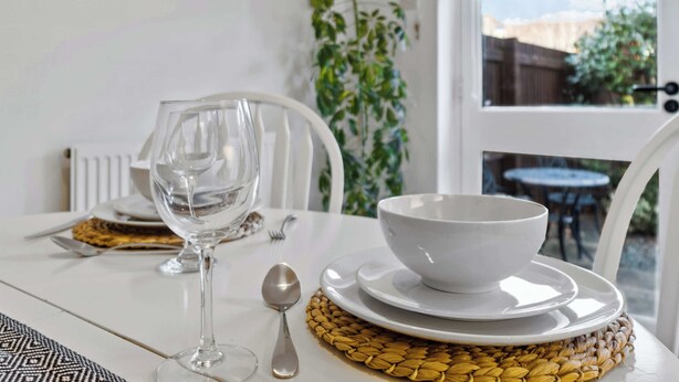 A dining table with a white bowl, a wine glass, and a spoon on a woven placemat. - Central Exeter 3BR | Walk Everywhere (Exeter)