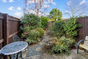 Enjoy a peaceful retreat in this serene garden, featuring lush greenery, a circular table, and a wooden bench.
