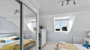 A modern bedroom with a large bed, a smaller bed, a walk-in closet, and a window with a view. - Central Exeter 3BR | Walk Everywhere (Exeter)