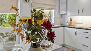 A dining area with a table set for two, a vase with flowers, and a view of the outdoors. - Central Exeter 3BR | Walk Everywhere (Exeter)