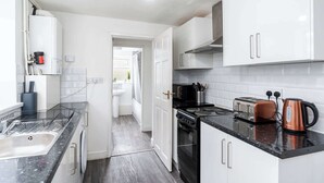 A modern kitchen with white cabinets, a black countertop, a stove, a sink, and a toaster. - Stylish 4BR Family Home | Heart of Grimsby (Grimsby)